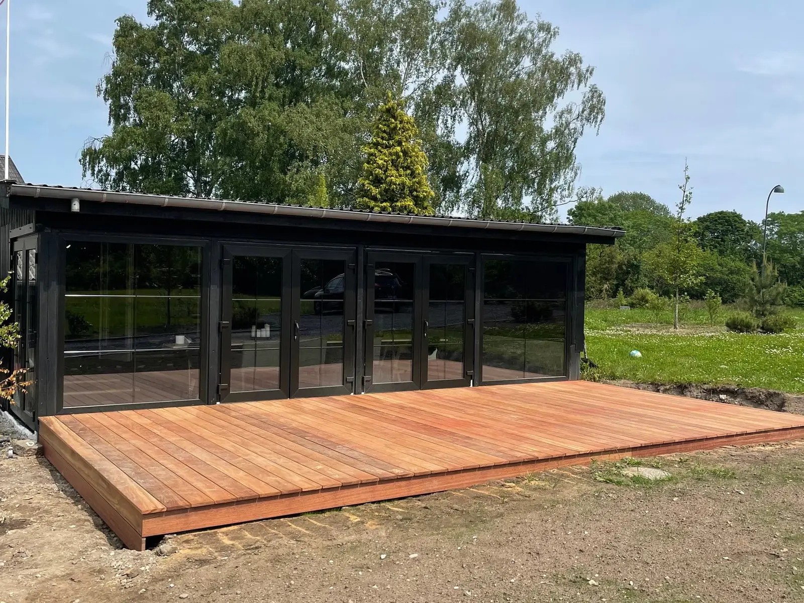Bred træterrasse foran et sort træhus